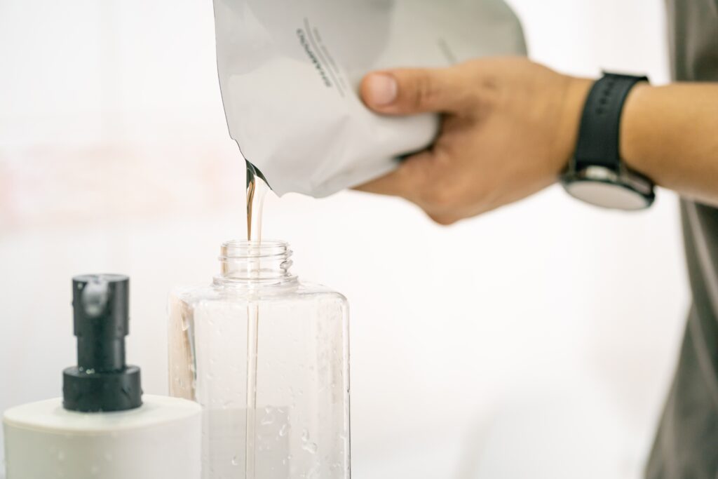 Persona rellenando un dispensador de jabón o champú desde un envase de recarga a envases rellenables